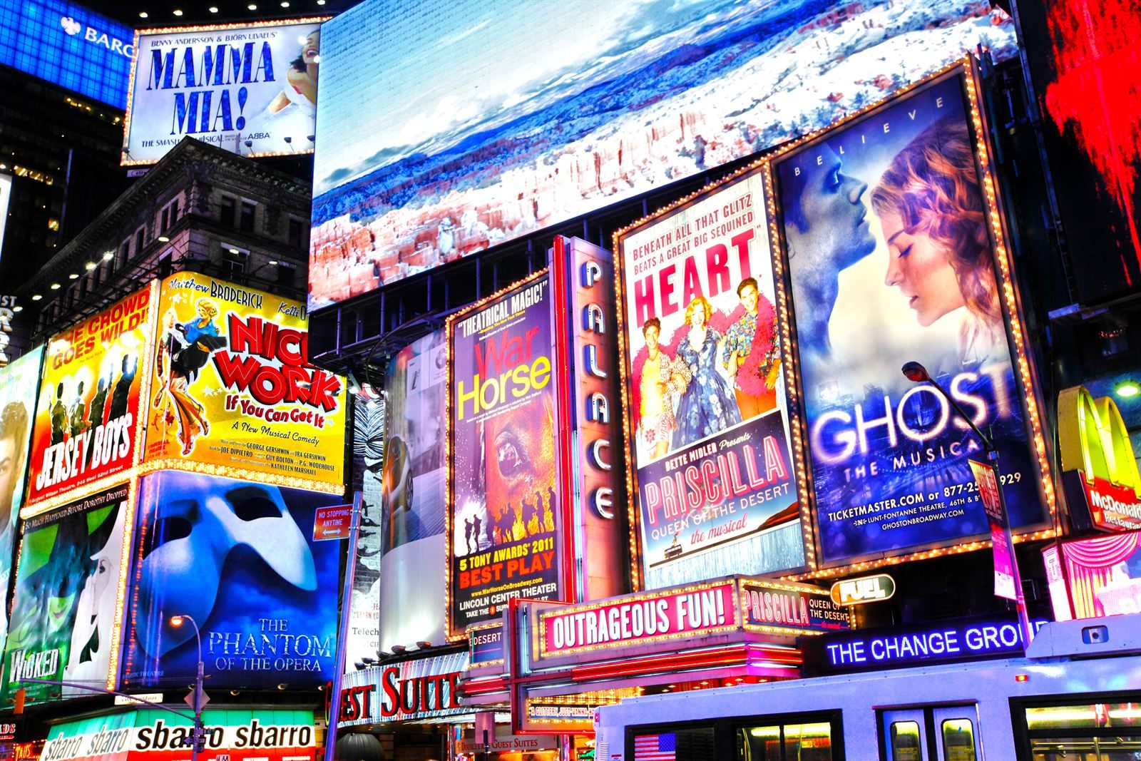 Illuminated Broadway show billboards stacked above a Times Square street