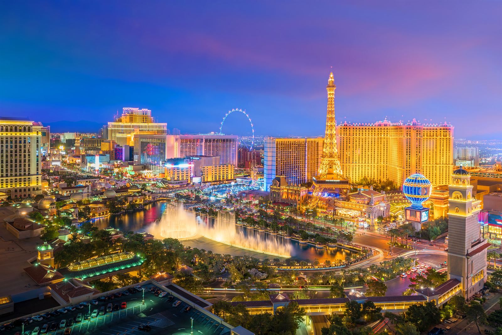 The Las Vegas Strip at dusk with lit fountains, resort towers and an Eiffel Tower replica